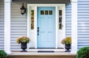 A beautiful front entrance of a house with baby blue siding and a sky blue door. Planters and columns frame the front steps.