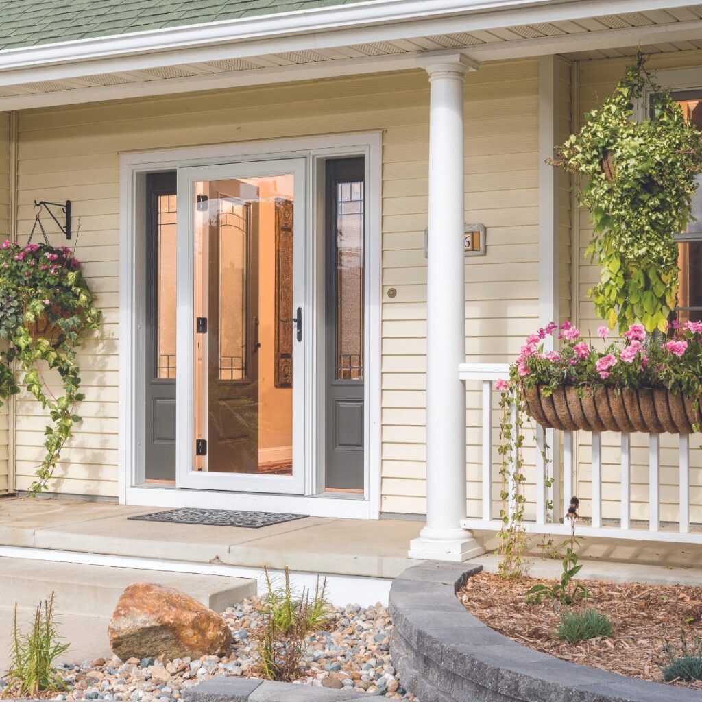 The front porch of a yellow house with a white storm door in front of a gray front door.